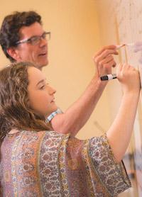 Student and professor writing on whiteboard